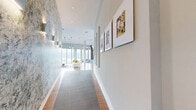 Located at 20 Water Grant St in Yonkers, NY, this generously scaled amenity space offers a sophisticated blend of modern design and waterfront living. The interior living area is anchored by warm hardwood flooring, soaring ceilings, and floor-to-ceiling windows that frame sweeping views of the Hudson River and surrounding waterfront grounds. Contemporary pendant lighting and curated wall art add a vibrant, artistic character throughout.

A stylish lounge and bar area features a striking teal tile backdrop with arched detailing, a long marble-topped island with sleek white tulip seating, and intimate booth-style banquettes, creating an upscale social atmosphere. An adjacent game room energizes the space with bold, colorful murals, arcade machines, a foosball table, and a pool table, making it an entertainment destination in its own right.

The expansive outdoor terraces are a true highlight, finished with composite deck tiles and fitted with glass-panel railings that preserve unobstructed panoramic views of the Hudson River. Multiple seating areas with navy blue outdoor sofas, a pergola with string lighting, and an outdoor bar make the terraces ideal for gatherings. Ceiling fans beneath covered overhangs and clean modern architecture complete this exceptional waterfront amenity space.