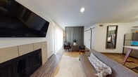 This thoughtfully designed single-floor residence blends contemporary style with warm, functional living. The living room serves as the centerpiece, featuring a sleek tile-surround fireplace, a wall-mounted TV, and sheer floor-to-ceiling curtains that invite natural light. A distinctive vertical slat room divider adds an architectural focal point, visually separating the seating area while maintaining an open feel. Rich wood-look flooring runs throughout, grounding the space with warmth and continuity.

The kitchen is well-equipped with sage-green cabinetry, granite-look countertops, and a full suite of stainless steel appliances including a refrigerator, dishwasher, microwave, and range. A compact dining area with a white table and bar-height seating provides a practical everyday dining solution adjacent to the kitchen.

The bedroom offers a calm, intimate retreat with warm pendant lighting, a wood-framed bed, and tasteful wall art that contributes to a relaxed, modern aesthetic. The bathroom continues the cohesive design language with green-toned cabinetry, granite countertops, wood-look flooring, and a full-length mirror that enhances the sense of space. Each area of this residence reflects a consistent mid-century modern sensibility with carefully curated finishes throughout.