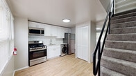 This two-story home in Halethorpe, MD offers a thoughtfully designed layout spread across two floors. The main level hosts the kitchen and living area, while the upper floor is dedicated to the bedrooms and bathroom, connected by a staircase with a bold black railing.

The kitchen is a standout feature, outfitted with crisp white shaker cabinets, a classic white subway tile backsplash, stainless steel appliances including a gas range, over-the-range microwave, and refrigerator, as well as a convenient in-unit washer. Light wood-style flooring runs throughout the main level, lending warmth and a clean, contemporary feel. A window allows natural light to brighten the kitchen and dining area.

Upstairs, two carpeted bedrooms offer comfortable retreats, each finished with neutral tones and windows that bring in natural light and outdoor views. One bedroom includes built-in closet shelving, adding useful storage. A hallway connects the bedrooms to the full bathroom, which features a tub/shower combination, wood-style flooring, and a clean white finish throughout.

Overall, the space maintains a consistent, modern aesthetic with neutral walls, clean white trim, and practical finishes that create a bright and functional living environment.