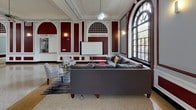 Located at 1700 E 56th St in Chicago's Hyde Park neighborhood, this single-floor facility showcases classic institutional architecture with striking character throughout. The centerpiece is a grand, open hall distinguished by soaring arched windows with dark steel mullions, ornate white crown molding, and deep burgundy accent walls that lend a sense of historic grandeur. Polished terrazzo floors with inlaid gold banding run the length of the main hall, reflecting abundant natural light that pours in from the oversized arched windows framing views of the surrounding greenery.

The main hall is thoughtfully divided into functional zones: a lounge area furnished with large sectional sofas and a presentation screen for gatherings or screenings, and a recreation area outfitted with ping-pong tables, a foosball table, arcade games, and a piano. Structural columns punctuate the space while preserving its open, airy feel, and ceiling fans add to the comfort of the hall.

The fully equipped communal kitchen features granite countertops, white cabinetry, gas ranges, overhead ventilation hoods, and individual storage lockers, complemented by a separate room lined with multiple full-size refrigerators for additional cold storage. A dedicated bike storage room with racks accommodates cyclists with ease. Together, these amenities create a versatile, well-appointed community space.