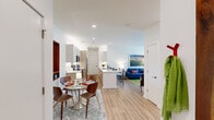 The Victor in Novi, Michigan presents a thoughtfully designed 1-bedroom, 1-bathroom residence that maximizes its generous floor plan through an open-concept layout. Light wood-tone flooring flows continuously throughout the space, creating visual cohesion from the entrance to the living areas.

The galley-style kitchen is a standout feature, outfitted with dual-tone cabinetry combining white upper cabinets and warm wood lower cabinets, sleek quartz countertops, under-cabinet lighting, and stainless steel appliances. A central island with a undermount sink provides additional workspace and a natural transition into the dining area, where a circular glass-top table anchors the space.

Two distinct living areas offer versatile functionality — one serves as a relaxed lounge with access to an outdoor patio door framing lush greenery, while the second adapts well as a home office or sitting room. Both benefit from recessed lighting and clean white walls.

The bedroom is a calm retreat with natural light from a large window, direct access to the bathroom, and ample space for a full furniture arrangement. The bathroom features a glass-enclosed shower, floating vanity with white cabinetry, and matching wood-tone flooring, maintaining the modern aesthetic found throughout the residence.