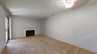 Located at 6747 W Par Ln in Wichita, Kansas, this single-floor, one-bedroom, one-bathroom unit offers a compact and efficiently designed layout. The living room serves as the heart of the space, featuring a classic fireplace with a white mantel, soft wall-to-wall carpeting in a warm neutral tone, a textured popcorn ceiling, and a ceiling fan light fixture. A sliding glass door brings in natural light and adds a sense of openness. A pass-through window connects the living area to the kitchen, which is equipped with dark cabinetry, a built-in microwave, and a white refrigerator, offering a practical and space-conscious design. The bedroom is a well-proportioned, carpeted room with soft grey walls, a textured ceiling, and a window with blinds that allows natural light to filter in. A dedicated closet provides additional storage. The bathroom features wood-look vinyl flooring, a dark-toned vanity with a single sink, a wall-mounted medicine cabinet mirror, and a full tub-shower combo with a curved curtain rod. Throughout the unit, neutral grey walls and consistent flooring choices create a clean, cohesive aesthetic suited for comfortable everyday living.