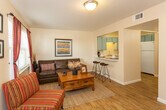 Located at 2100 E Tenth St in Odessa, Texas, this single-floor unit offers a well-organized and functional layout designed for comfortable everyday living. The living room serves as the heart of the space, featuring warm wood-look flooring, a large window that invites natural light, and a cozy atmosphere anchored by a leather sectional sofa and a solid wood coffee table. A pass-through opening connects the living area to the kitchen, complete with bar seating — an ideal setup for casual dining or entertaining. The kitchen is efficiently designed in a U-shaped layout, outfitted with distinctive teal cabinetry, light-toned countertops, a double-basin sink, and white appliances including a refrigerator, range, and dishwasher. The bedroom provides a quiet retreat, featuring the same wood-look flooring and wall space suited for personal décor. The bathroom area includes a dedicated vanity with teal-toned cabinetry, a framed mirror, and light countertops, with access to a closet and separate toilet room for added convenience. Throughout the unit, consistent flooring and a neutral color palette create a cohesive and inviting atmosphere.