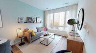 Located at 165 Huguenot Street in New Rochelle, NY, this single-floor residence offers a well-designed, contemporary living experience. The open-concept layout connects the living, dining, and kitchen areas seamlessly, creating a cohesive and functional flow throughout the space.

The living area is distinguished by soft seafoam-blue accent walls, warm hardwood-style flooring, and a large picture window that invites abundant natural light and urban views. A picture ledge display shelf adds a curated, gallery-like touch above a comfortable seating arrangement centered around a sleek coffee table.

The kitchen is thoughtfully appointed with two-tone cabinetry — crisp white lower cabinets paired with charcoal upper cabinets — stainless steel appliances, open display shelving, and a white waterfall-edge island with bar seating, ideal for casual dining or meal prep. Adjacent to the kitchen, a compact dining nook provides additional seating for everyday meals.

The bedroom is a serene retreat, featuring a large window with city views, soft neutral tones, built-in closet storage, and warm accent lighting. The bathroom presents a clean, minimalist aesthetic with light tile flooring, a white vanity with an undermount sink, and a large frameless mirror. Throughout the residence, modern finishes and a neutral palette create a polished and inviting atmosphere.