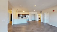 This single-floor residence offers a thoughtfully designed open-concept layout that seamlessly connects the living area, dining space, and kitchen. Wide-plank hardwood-style flooring flows throughout the main living areas, contributing to a cohesive and contemporary aesthetic.

The kitchen is well-appointed with dark espresso cabinetry, a mosaic tile backsplash, and a full suite of stainless steel appliances, including a French door refrigerator with ice and water dispenser, an electric range, and an over-the-range microwave. A large central island with a white countertop and undermount sink provides additional workspace and casual seating opportunities, with pendant lighting overhead adding a refined finishing touch.

The spacious living area benefits from natural light streaming in through large windows and a sliding glass door that leads to a private balcony. A dedicated in-unit laundry area houses a stacked washer and dryer. A walk-in closet provides generous storage. The bathroom features tile flooring, a sliding frosted-glass shower enclosure, a dark-cabineted vanity with a white countertop, and a full mirror. Additional hallway access connects the bedroom to the bathroom for added convenience.