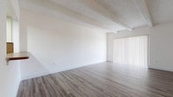 This single-floor unit offers a clean, neutral aesthetic throughout, characterized by crisp white walls and an open, airy feel. The main living area is spacious and welcoming, featuring wood-look plank flooring and a distinctive textured ceiling with exposed decorative beams that add architectural character. Vertical blinds over a sliding door allow for natural light control while providing access to the outdoors.

The kitchen is laid out in a functional U-shape, equipped with white cabinetry offering generous storage, a tile backsplash, laminate countertops, a coil-burner electric range, dishwasher, and a stainless steel sink — all finished with the same wood-look flooring that runs through the living areas.

The bedrooms are comfortably sized, each featuring soft neutral carpeting, exposed beam ceilings, and vertical blinds over windows that bring in natural light. Multiple bifold closet doors in each bedroom provide substantial built-in storage. The primary bedroom includes access to a dedicated closet area and connects conveniently to the hallway.

The bathroom is finished in clean white tile flooring and features a full tub-shower combination, a white vanity with a single sink, and a large mirror — creating a bright and functional space. The overall ambiance of the unit is clean, minimal, and move-in ready.