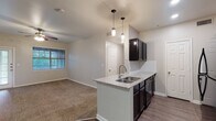 This single-floor residence offers a thoughtfully designed open-concept layout that seamlessly connects the kitchen, dining, and living areas. The kitchen serves as a central focal point, featuring dark cabinetry, granite countertop surfaces, a peninsula with a double-basin sink, and sleek pendant lighting overhead. Black appliances, including a refrigerator and range, complement the bold cabinetry tones. Wood-look plank flooring runs through the kitchen and main living areas, providing a clean contrast to the neutral wall tones throughout.

The living area is generously proportioned, with carpet flooring, ceiling fans, and access to natural light through slatted blinds. A dedicated entryway with a paneled front door and secondary glass-paned door offers practical access points to the space.

The bedrooms continue the carpeted, neutral aesthetic, each outfitted with ceiling fans and windows that bring in natural light. Both bathrooms are finished with granite-topped dark vanities, large framed mirrors, wood-look flooring, and tub-shower combinations with tile accents, ensuring a consistent and polished look throughout. The overall design balances functionality with modern finishes, creating a cohesive and comfortable living environment.