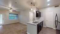 This single-floor residence offers a thoughtfully designed open-concept layout that seamlessly connects the kitchen, dining, and living areas. The kitchen serves as a central focal point, featuring dark cabinetry, granite countertop surfaces, a peninsula with a double-basin sink, and sleek pendant lighting overhead. Black appliances, including a refrigerator and range, complement the bold cabinetry tones. Wood-look plank flooring runs through the kitchen and main living areas, providing a clean contrast to the neutral wall tones throughout.

The living area is generously proportioned, with carpet flooring, ceiling fans, and access to natural light through slatted blinds. A dedicated entryway with a paneled front door and secondary glass-paned door offers practical access points to the space.

The bedrooms continue the carpeted, neutral aesthetic, each outfitted with ceiling fans and windows that bring in natural light. Both bathrooms are finished with granite-topped dark vanities, large framed mirrors, wood-look flooring, and tub-shower combinations with tile accents, ensuring a consistent and polished look throughout. The overall design balances functionality with modern finishes, creating a cohesive and comfortable living environment.