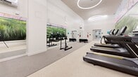 Located at 1170 Hancock St in Quincy, Massachusetts, this well-appointed fitness center offers a generously sized, single-floor space designed with both functionality and aesthetics in mind. The room features soaring ceilings that amplify the sense of openness, complemented by sleek circular pendant lighting that adds a contemporary touch to the bright, white interior. A striking large-scale nature mural spans a prominent wall, depicting lush greenery and a colorful sky, creating an energizing and visually immersive environment for workouts. Durable, light-colored terrazzo-style flooring runs throughout, providing a clean and practical surface for exercise. The space is equipped with an impressive array of cardio machines, including treadmalls, ellipticals, and stationary bikes, as well as strength and functional training equipment such as sled trainers and stability accessories. A full-length mirror along one wall enhances the sense of depth and allows for form monitoring during exercise. A metal staircase with sleek railings connects to an adjacent area, adding a multi-level dimension to the facility. Glass-paneled doors provide natural light and easy access, rounding out a fitness space that balances modern design with practical, high-quality amenities.