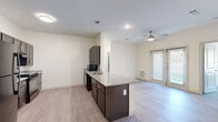 This single-floor residence offers a thoughtfully designed layout across a comfortable footprint, accommodating two bedrooms and two full bathrooms. The open-concept kitchen and living area forms the heart of the home, where a peninsula with granite countertops and dark espresso cabinetry defines the kitchen space. Black appliances, including a refrigerator, range, and built-in microwave, complement the cabinetry, while light wood-style flooring extends throughout the main living area, creating a cohesive and modern aesthetic. A ceiling fan and access to a glazed exterior door bring natural light and ventilation into the living room.

Both bedrooms are well-proportioned, with the primary bedroom offering generous space. Each room features ceiling fans, light wood-style flooring, and windows with outdoor views. The two bathrooms are distinctly appointed: one is accessibility-friendly, featuring grab bars, an open vanity with granite countertops, and large-format tile flooring, while the second bathroom includes a walk-in glass-enclosed shower and navy cabinetry with granite countertops. A dedicated closet provides additional storage. The overall ambiance is clean, modern, and functional.