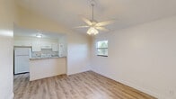 Located in Hobe Sound, Florida, this single-story, one-bedroom, one-bathroom unit offers a bright and clean living environment with a thoughtfully efficient layout. Light wood-look flooring runs throughout, lending warmth and continuity across every room.

The combined kitchen and living area serves as the heart of the home. The living space features a ceiling fan with light fixture and a window that brings in natural light and outdoor views of surrounding greenery. A wall-unit air conditioner ensures year-round comfort. The kitchen is well-equipped with white shaker cabinetry, granite-style countertops, a stainless steel sink, a white refrigerator, and an electric range — all complemented by a pass-through counter that connects seamlessly to the living area.

The bedroom is a comfortable, well-proportioned retreat with its own ceiling fan, a window overlooking the outdoors, and direct access to a generously sized walk-in closet outfitted with wire shelving and hanging rods on multiple sides, providing excellent storage capacity.

The bathroom includes a full tub-shower combination with chrome fixtures set against clean white surroundings. A utility room and hallway round out the floorplan, adding practical functionality. The overall ambiance is clean, move-in ready, and filled with natural light.