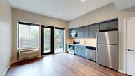 Located at 590 Park St in Saint Paul, Minnesota, this thoughtfully designed studio unit offers a contemporary living experience within a compact, single-floor layout. The open-concept kitchen and living area serves as the heart of the space, finished with warm wood-look luxury vinyl plank flooring that runs throughout. The kitchen is outfitted with sleek, blue-gray flat-front cabinetry extending to the ceiling for ample storage, complemented by a white subway tile backsplash, light countertops, and a full suite of stainless steel appliances including a refrigerator, electric range, built-in microwave, and dishwasher. The living area benefits from a sliding glass door that floods the room with natural light and provides direct access to an outdoor area, while a wall-mounted HVAC unit ensures year-round comfort. A short hallway leads from the main living space to the full bathroom, which features a tub-shower combination, a vanity with under-cabinet storage, and a large mirror. The hallway also includes convenient wall-mounted coat hooks. Clean neutral walls, recessed lighting, and black hardware accents throughout give the unit a polished, modern aesthetic suited for contemporary urban living.