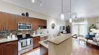 Located at 925 S Main St in Grapevine, Texas, this well-appointed one-bedroom, one-bathroom residence offers a smart, efficient layout across a single floor. The open-concept kitchen and living area serves as the heart of the home, where rich dark wood cabinetry, granite countertops, a mosaic tile backsplash, and a full suite of stainless steel appliances create a polished culinary space. A peninsula with a granite overhang provides additional prep and seating space. Warm hardwood flooring flows throughout the main living areas, anchoring the bright and airy living room, which is highlighted by crown molding, elevated ceilings, and a set of French doors that flood the space with natural light and offer views of the outdoors. The bedroom is a comfortable retreat featuring plush carpet, a ceiling fan, and generous windows that invite soft, natural light. The full bathroom is appointed with rich cabinetry, a granite vanity with dual sinks, and a tub-shower combination with tile surround. A hallway connects the rooms efficiently and includes access to an in-unit washer and dryer closet, adding everyday convenience. Crown molding details and neutral tones throughout lend the space a cohesive, refined character.