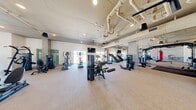 Located at 3240 W Harmon Ave in Las Vegas, NV, this professionally equipped fitness center offers a spacious, single-floor layout designed to accommodate a wide variety of workout routines. The open floor plan spans a generous footprint, providing ample room for both individual training and group exercise without feeling overcrowded.

The facility features an extensive selection of strength and conditioning equipment, including cable machines, multi-functional cable stations, weight benches, and free weights. A dedicated functional training zone is outfitted with a heavy bag, battle ropes, a power rack, and a rowing machine, catering to high-intensity and cross-training workouts. The cardio section lines the perimeter with treadmills, ellipticals, stair climbers, and stationary bikes, many positioned to take advantage of the large windows.

Architecturally, the space features exposed ductwork and piping along the ceiling, lending it an industrial aesthetic complemented by clean white walls, stone-clad structural columns, and light neutral flooring throughout. Recessed lighting and ceiling fans maintain a bright and comfortable environment. Large windows along multiple walls flood the interior with natural light and offer views of the surrounding Las Vegas skyline. Full-length mirrors are strategically placed to enhance the sense of space and support proper form during training.