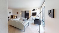 This contemporary single-floor residence showcases a thoughtfully designed open-concept layout that seamlessly integrates the living, dining, and kitchen areas. Light-toned hardwood flooring runs throughout the main living space, complementing the clean white walls and creating a bright, airy atmosphere. Floor-to-ceiling windows frame expansive urban views, flooding the space with natural light.

The kitchen features sleek, light wood cabinetry paired with dark countertops and modern pendant lighting above a substantial wooden dining table. The open design allows for effortless flow between cooking, dining, and entertaining areas.

The bedrooms are accessed through tall, elegant white doors with warm wood-toned hardware. Both rooms feature plush neutral carpeting and large windows offering city views. The primary bedroom is generously proportioned, with carefully placed wall-mounted lighting flanking a textured upholstered headboard.

The ensuite bathroom is a standout feature, showcasing wood-look porcelain tile flooring, a sleek floating vanity, and a spacious walk-in shower fully lined with square mosaic tiles behind frameless glass enclosures. A separate water closet with open shelving completes the bathroom suite. Throughout the residence, the design palette of neutrals, natural wood tones, and clean lines creates a cohesive, sophisticated ambiance.
