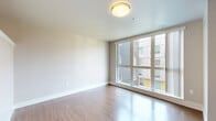 Located at 315 First Ave N in Seattle's Lower Queen Anne neighborhood, this single-floor unit offers a well-designed layout that makes smart use of its compact footprint. The combined kitchen and living area forms the heart of the space, anchored by warm hardwood-style flooring that runs throughout. A large picture window in the living area floods the room with natural light and frames views of the surrounding neighborhood, creating an open and airy atmosphere.

The kitchen is outfitted with stainless steel appliances, including a range, over-the-range microwave, dishwasher, and full-size refrigerator. Warm wood-toned cabinetry extends floor to ceiling, providing generous storage, while a light-toned countertop with an undermount sink completes the functional galley-style setup. Track lighting overhead adds a modern touch.

The bathroom features matching wood-toned cabinetry with a wide vanity, white countertop, an extended wall mirror, and a full tub/shower combination. Light gray tile flooring lends a clean, contemporary finish.

A dedicated closet provides additional storage, and the hallway connecting the living spaces offers a clean, well-lit transition throughout the unit. The consistent use of warm wood finishes, neutral wall tones, and modern hardware gives the entire space a cohesive and contemporary character.