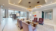 Located at 2925 Buford Dr in Buford, Georgia, this two-story amenity center delivers a polished, contemporary design across a generously scaled layout. The ground floor makes an immediate impression with large-format white tile flooring, soaring ceilings, and a dramatic open-riser staircase with glass railings that anchors the space visually. A welcoming lounge area features a coffered ceiling with eye-catching circular gold pendant fixtures, plush seating arrangements, and abundant natural light filtered through oversized windows.

Adjacent to the lounge, a stylish café-style bar showcases teal cabinetry, a curved white countertop, brass pendant lighting, and mirrored backwall detailing — creating an upscale social hub. A dedicated media lounge offers deep-cushioned seating, warm wood slatted accent walls, teal feature walls, and curated artwork.

The second floor opens to a bright, airy lounge and co-working area defined by a striking wood slatted ceiling canopy, built-in booth seating, bar-height tables, and views of the surrounding community and pool courtyard below through expansive floor-to-ceiling windows. A glass-enclosed fitness center is conveniently accessible from the upper-level corridor, offering visibility and easy access throughout.