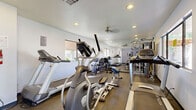 Located at 4101 W Union Hills Dr in Phoenix, AZ, this fitness center is a single-floor exercise facility designed to support a variety of workout routines. The space features durable flooring suited for high-traffic use, white walls, and recessed lighting that keeps the room well-lit throughout. A ceiling fan contributes to air circulation during workouts.

The room is outfitted with an array of cardio equipment, including multiple treadmills and elliptical machines, as well as a stationary recumbent bike. A multi-station cable machine provides options for strength training, and a set of free weights along with a weight bench add further versatility for resistance exercises. Full-length mirrors line one wall, visually expanding the space and allowing users to monitor their form.

Natural light filters in through several windows, offering views of the surrounding outdoor area and contributing to an energizing atmosphere. Motivational phrases are displayed on the walls, reinforcing a focused fitness environment. A fire extinguisher and posted exercise room rules reflect attention to safety and facility management. The space is accessed through a single entry door, keeping the area self-contained and functional for dedicated exercise use.