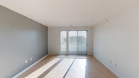 This well-designed single-floor residence offers a clean, modern aesthetic with a thoughtful layout that balances functionality and comfort. The open living area immediately impresses with its light hardwood flooring, neutral gray accent walls, and large sliding glass doors fitted with horizontal blinds, allowing abundant natural light to pour in while providing a view to the outdoors. The contemporary kitchen is a standout feature, showcasing dark espresso cabinetry that reaches toward the ceiling, stainless steel appliances including a refrigerator, range, and microwave, complemented by light quartz countertops and a subway tile backsplash. Stylish pendant lighting adds a finishing touch over the kitchen island, which also features an integrated sink. The bedroom is a comfortable retreat, finished with plush wall-to-wall carpeting, multiple windows dressed with blinds for natural light control, and a ceiling fan for year-round comfort. The full bathroom is appointed with light hardwood-style flooring, dark wood vanity cabinetry with a clean white countertop, a full-size soaking tub with shower, and crisp white walls that contribute to a bright, spa-like feel. Throughout, the consistent use of neutral tones, quality materials, and modern fixtures creates a cohesive and inviting atmosphere.