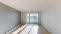This well-designed single-floor residence offers a clean, modern aesthetic with a thoughtful layout that balances functionality and comfort. The open living area immediately impresses with its light hardwood flooring, neutral gray accent walls, and large sliding glass doors fitted with horizontal blinds, allowing abundant natural light to pour in while providing a view to the outdoors. The contemporary kitchen is a standout feature, showcasing dark espresso cabinetry that reaches toward the ceiling, stainless steel appliances including a refrigerator, range, and microwave, complemented by light quartz countertops and a subway tile backsplash. Stylish pendant lighting adds a finishing touch over the kitchen island, which also features an integrated sink. The bedroom is a comfortable retreat, finished with plush wall-to-wall carpeting, multiple windows dressed with blinds for natural light control, and a ceiling fan for year-round comfort. The full bathroom is appointed with light hardwood-style flooring, dark wood vanity cabinetry with a clean white countertop, a full-size soaking tub with shower, and crisp white walls that contribute to a bright, spa-like feel. Throughout, the consistent use of neutral tones, quality materials, and modern fixtures creates a cohesive and inviting atmosphere.