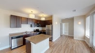 Located at 250 Summit Blvd in Broomfield, Colorado, this single-floor residence offers a well-designed, open-concept layout with modern finishes throughout. The kitchen serves as the heart of the home, outfitted with rich dark-walnut cabinetry, stainless steel appliances including a refrigerator, range, microwave, and dishwasher, and a central island with a neutral stone-toned countertop. Pendant drum lighting adds a polished touch above the island, while light hardwood-style flooring flows seamlessly into the adjacent living area, which is bright and open with clean, neutral walls. The bedrooms are carpeted for comfort and feature ceiling fans and generous natural light courtesy of multiple windows with outdoor views. One bedroom includes built-in shelving, making it well-suited as a secondary bedroom or home office, while another bedroom provides direct access to a walk-in closet. The bathroom is finished with dark wood cabinetry, a wide vanity mirror with backlit fixtures, wood-style tile flooring, and a tiled shower surround. Throughout the space, crisp white trim, neutral wall tones, and consistent flooring choices create a cohesive, contemporary aesthetic suited for modern living.