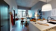 Located in Chicago's vibrant West Loop neighborhood, this contemporary residence at 34–68 N Peoria St showcases an impressive industrial-modern aesthetic defined by exposed concrete ceilings and an open, airy layout. The living area is a standout, featuring dramatic floor-to-ceiling windows that flood the space with natural light and frame breathtaking views of the Chicago skyline. A tufted navy sofa, sculptural coffee table, and wall-mounted media console anchor the room, while a lean black shelving unit adds both style and function. The open-plan dining area accommodates a round pedestal table with mid-century modern chairs, seamlessly connecting to the kitchen. The kitchen is outfitted with stainless steel appliances, including a full-sized refrigerator and gas range, dark cabinetry, and a clean white countertop peninsula. The bedroom offers a serene retreat with large windows continuing the skyline panorama, complemented by warm, neutral tones and ample space. The bathroom features large-format tile, a soaking tub with shower combination, a dark-vanity with an illuminated mirror, and refined fixtures throughout. The overall ambiance balances urban energy with refined comfort.