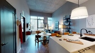 Located in Chicago's vibrant West Loop neighborhood, this contemporary residence at 34–68 N Peoria St showcases an impressive industrial-modern aesthetic defined by exposed concrete ceilings and an open, airy layout. The living area is a standout, featuring dramatic floor-to-ceiling windows that flood the space with natural light and frame breathtaking views of the Chicago skyline. A tufted navy sofa, sculptural coffee table, and wall-mounted media console anchor the room, while a lean black shelving unit adds both style and function. The open-plan dining area accommodates a round pedestal table with mid-century modern chairs, seamlessly connecting to the kitchen. The kitchen is outfitted with stainless steel appliances, including a full-sized refrigerator and gas range, dark cabinetry, and a clean white countertop peninsula. The bedroom offers a serene retreat with large windows continuing the skyline panorama, complemented by warm, neutral tones and ample space. The bathroom features large-format tile, a soaking tub with shower combination, a dark-vanity with an illuminated mirror, and refined fixtures throughout. The overall ambiance balances urban energy with refined comfort.