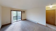 This 1-bedroom, 1-bathroom unit is thoughtfully laid out across a single floor, offering a practical and comfortable living environment. The carpeted living room is bright and open, featuring a sliding glass door that leads to a private balcony overlooking lush greenery, filling the space with natural light. A wall-mounted air conditioning unit and baseboard heating ensure year-round comfort. The kitchen is accessed through a pass-through window from the living area and features warm honey-toned cabinetry, granite-style countertops, a gas range, and a full-size refrigerator, all set over easy-clean tile flooring. The bedroom is generously proportioned with plush carpeting, a window with blinds for natural light and privacy, and direct access to both a walk-in closet and the full bathroom. The bathroom is clean and functional, equipped with a single vanity, a full tub-shower combination, and tile flooring. Throughout the unit, wood-trimmed doorways, neutral wall tones, and consistent finishes create a cohesive and inviting atmosphere that is move-in ready.