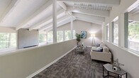 Located at 2954 Columbiana Ct in Vestavia Hills, Alabama, this single-floor space offers a thoughtfully designed layout encompassing a living room and dining room. The architecture is defined by dramatic vaulted ceilings with striking exposed white wood beams and white-painted tongue-and-groove paneling above, lending a bright, airy character throughout.

The living room is a welcoming, open area where an abundance of natural light pours in through a continuous row of windows along the wall, framing serene, wooded views. The high-pitched ceiling amplifies the sense of openness, while patterned carpet in muted tones grounds the space with a comfortable, modern feel.

The dining room continues the same architectural language, featuring soaring vaulted ceilings and expansive sliding glass windows that offer unobstructed views of the surrounding mature tree canopy. Natural light floods this room generously, creating a tranquil, nature-connected atmosphere well-suited for gatherings.

Throughout the space, neutral warm-gray wall tones complement the crisp white ceiling structures, contributing to a cohesive and polished aesthetic. The consistent use of patterned carpet, clean lines, and mid-century-influenced design details ties both rooms together harmoniously. The overall ambiance is calm, bright, and inviting, with the lush Alabama landscape serving as a natural backdrop at every turn.