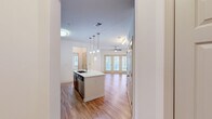 Located at 30 Gates Mill St in Huntsville, Alabama, this well-designed one-bedroom, one-bathroom residence offers a smart, functional layout across a single floor. The open-concept living and kitchen area serves as the heart of the home, featuring warm hardwood-style flooring that flows throughout the main living spaces. The kitchen is equipped with rich dark-wood cabinetry, a white quartz countertop island with a deep double-basin sink, stainless steel appliances including a refrigerator, range, and microwave, and a classic subway tile backsplash. Pendant lighting above the island adds a polished finishing touch. The living room is bright and airy, benefiting from natural light streaming through a set of French doors, and is completed by a ceiling fan overhead. The bedroom offers plush carpeting, its own ceiling fan, and direct access to a walk-in closet outfitted with wire shelving for organized storage. The full bathroom features dark wood vanity cabinetry, a white quartz countertop with an undermount sink, a large mirror, and a tub-shower combination with clean white surround. The entrance and hallway connect each space efficiently, making the overall layout feel cohesive and practical throughout.