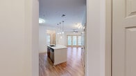 Located at 30 Gates Mill St in Huntsville, Alabama, this well-designed one-bedroom, one-bathroom residence offers a smart, functional layout across a single floor. The open-concept living and kitchen area serves as the heart of the home, featuring warm hardwood-style flooring that flows throughout the main living spaces. The kitchen is equipped with rich dark-wood cabinetry, a white quartz countertop island with a deep double-basin sink, stainless steel appliances including a refrigerator, range, and microwave, and a classic subway tile backsplash. Pendant lighting above the island adds a polished finishing touch. The living room is bright and airy, benefiting from natural light streaming through a set of French doors, and is completed by a ceiling fan overhead. The bedroom offers plush carpeting, its own ceiling fan, and direct access to a walk-in closet outfitted with wire shelving for organized storage. The full bathroom features dark wood vanity cabinetry, a white quartz countertop with an undermount sink, a large mirror, and a tub-shower combination with clean white surround. The entrance and hallway connect each space efficiently, making the overall layout feel cohesive and practical throughout.