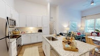 This single-floor residence is thoughtfully designed with a clean, contemporary aesthetic carried consistently throughout each room. The kitchen serves as a central highlight, featuring crisp white shaker cabinetry extending to the ceiling for generous storage, granite countertops, a large island with an undermount sink, and a full suite of stainless steel appliances including a refrigerator, range, and built-in microwave. Wood-look flooring runs through the kitchen and main living areas, adding warmth to the bright, white interior.

The living room offers a comfortable, light-filled setting with large windows and a glass-paneled door that invite natural light and provide views of lush outdoor greenery. The open layout connects the kitchen and living areas seamlessly, enhancing the sense of spaciousness.

Two well-proportioned bedrooms each feature plush carpeting and large windows that bring in natural light. Both bathrooms are finished with matching granite-topped white vanities. The primary bathroom includes a walk-in glass shower, while the secondary bathroom features a full soaking tub with shower combination. Wood-look flooring is carried into both bathrooms, maintaining a cohesive design throughout the residence.