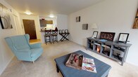 This 1-bedroom, 1-bathroom residence is thoughtfully laid out across a single floor, offering a practical and comfortable living experience. The open living room is generously sized, featuring plush wall-to-wall carpeting, neutral white walls, and large windows that invite natural light and provide pleasant outdoor views of surrounding greenery. The living area flows seamlessly toward the kitchen, which is accessible via a breakfast bar with barstool seating — an ideal spot for casual dining or entertaining.

The galley-style kitchen is efficiently organized, featuring wood-toned cabinetry, laminate wood flooring, a full suite of white appliances including a stove and refrigerator, a stainless steel sink, and warm countertops. A dishwasher is also included, adding everyday convenience.

The bedroom is a serene retreat, with soft carpeting, bright windows overlooking lush outdoor scenery, and ample closet space behind louvered bifold doors. The clean, neutral palette throughout the room promotes a calm and restful atmosphere.

The bathroom is neatly appointed with a full soaking tub and shower combo, accented by classic white tile surround. Overall, this unit delivers a cohesive, move-in-ready living space with a functional layout and a warm, understated aesthetic throughout.