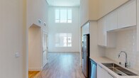 This thoughtfully designed two-floor loft-style residence makes an immediate impression with its dramatic double-height ceilings in the main living area, which flood the space with natural light through oversized stacked windows. The open-concept ground floor seamlessly connects the living area to a sleek, modern kitchen outfitted with white flat-front cabinetry, stone countertops, a tile backsplash, and a full suite of stainless steel appliances including a gas range, built-in microwave, dishwasher, and French door refrigerator. Warm wood-tone flooring runs throughout the main level, complementing the clean, bright aesthetic. A glass door off the living area opens to an outdoor balcony, offering city and mountain views. The bathroom on the main level features a full soaking tub and shower combination, built-in wall shelving, and hardwood-style flooring. Upstairs, the second floor offers a versatile loft space with plush carpeting, recessed lighting, and multiple windows that continue to bring in natural light and outward-facing views. Additional rooms on this level include a private space with a closet and hardwood flooring, ideal for use as a bedroom or home office. The overall design is clean, modern, and airy throughout.