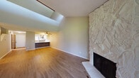 Located at 20554 NW Lapine Way in Portland, Oregon, this two-story home offers a thoughtfully designed layout with a range of functional and distinctive features. The main living area makes an immediate impression with its soaring vaulted ceiling, a large skylight that floods the space with natural light, and a floor-to-ceiling white stone fireplace that serves as a striking architectural focal point. Warm wood-look flooring extends throughout the main level, creating a cohesive and inviting atmosphere. The living area flows seamlessly into the kitchen, which is equipped with stainless steel appliances — including a refrigerator, range, and dishwasher — complemented by two-tone cabinetry featuring white upper cabinets and gray lower cabinets, white countertops, and a window overlooking lush greenery outside. A ceiling fan adds comfort to the transitional space between the kitchen and living area. The upper level includes a generously sized walk-in closet with built-in shelving, hanging rods, and carpeted flooring beneath a sloped roofline, offering ample storage. A full bathroom with a sliding-door shower enclosure, single vanity, and wood-look flooring provides practical convenience. The property also includes an attached single-car garage with a wood-paneled interior and concrete floor, offering secure parking and additional storage.