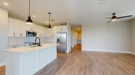 This thoughtfully designed single-floor home features three bedrooms, two bathrooms, and a functional layout that maximizes everyday livability. The open-concept living area is anchored by wood-look flooring, neutral walls, and multiple windows dressed with white blinds that bathe the space in natural light. A ceiling fan adds both style and comfort to the living room, which also provides access to a spacious screened porch overlooking the surrounding neighborhood and open skies — an ideal spot for outdoor relaxation. The kitchen is a standout feature, showcasing white shaker-style cabinetry, a classic subway tile backsplash, stainless steel appliances, and a center island with a matte black sink fixture and pendant lighting overhead. The primary bedroom is generously sized and includes a walk-in closet outfitted with wire shelving systems for ample organization. Additional bedrooms are carpeted with ceiling fans and natural light from windows, offering comfortable, quiet retreats. The bathrooms are finished with navy or white cabinetry, large vanity mirrors, white countertops, and tub-shower combinations with clean tile surrounds. Three closets are distributed throughout the home, providing excellent storage. The overall aesthetic is clean, modern, and move-in ready.