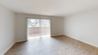 This single-story unit presents a clean, contemporary layout with consistent finishes throughout. The kitchen is accessed through an arched entryway and features gray shaker-style cabinetry, a white subway tile backsplash, a stainless steel sink, and black appliances including a refrigerator. Light wood-style luxury vinyl flooring runs through the kitchen and main living areas, providing a cohesive and easy-to-maintain surface.

The living area is open and well-lit, highlighted by large sliding glass doors fitted with vertical blinds that offer views of the surrounding outdoor space and allow generous natural light to fill the room. An adjacent dining area is defined by a pendant light fixture overhead, creating a functional and distinct space for meals.

The bedrooms are carpeted in neutral tones, offering a softer, quieter feel. Each room features white walls and access to additional areas of the unit. Natural light enters through standard windows with blinds.

The bathroom is finished with warm-toned large-format tile surrounding a full soaking tub and shower combination, complemented by chrome fixtures, a white vanity, and a textured ceiling. Overall, the unit presents a well-maintained, move-in ready space with a neutral palette throughout.