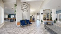 This single-floor community clubhouse offers a generously sized and thoughtfully designed amenity space that blends modern aesthetics with practical functionality. The main lounge area immediately impresses with its soaring vaulted ceilings clad in shiplap, striking marble-look tile flooring, and a bold white-painted brick column crowned by an oversized decorative clock — serving as the architectural centerpiece of the space. Plush seating, including tufted velvet chairs and chaise lounges in rich blues and grays with gold-accented frames, creates an inviting atmosphere throughout the open-plan layout. A dedicated game room features a full-size pool table and ping pong table set against deep slate-blue accent walls and French doors that invite natural light. Adjacent to the lounge, a fully appointed kitchen area with modern appliances and bar seating provides a convenient gathering spot. The fitness center is well-equipped with a full suite of cardio machines, strength training equipment, floor-to-ceiling mirrors, and patterned carpet flooring, all beneath a bright, recessed-lit shiplap ceiling. Gold-framed decorative shelving units and curated artwork add refined touches throughout, unifying the space with a cohesive, upscale residential feel.