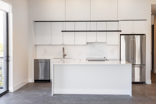 Signature Collection kitchen with white cabinetry, white marbled quartz countertop and backsplash, wine fridge, and upgraded stainless steel appliances - Avalon South Miami Apartments