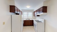 This single-floor unit offers a well-organized layout that maximizes functionality and livability. The interior is anchored by warm, richly toned hardwood floors that extend throughout the living and bedroom areas, lending a cohesive and inviting character to the space.

The kitchen is designed in a classic U-shape, featuring deep-toned dark wood cabinetry that provides generous storage both above and below the counters. White appliances — including a gas range with overhead ventilation hood and a full-size refrigerator — are neatly integrated into the layout. A single-basin sink is positioned beneath a double window, allowing natural light to brighten the workspace.

The living areas are open and airy, with clean white walls and multiple windows fitted with blinds that allow for adjustable natural light. Baseboard heating units are present throughout, ensuring consistent warmth. The rooms offer ample space for a variety of furniture arrangements.

The bathroom is finished in a clean, minimal style, featuring a full-size soaking tub with a shower fixture, neutral tile surround, and a window that provides natural ventilation and light.

Overall, the space presents a straightforward and practical floor plan with classic finishes, well-maintained hardwood flooring, and sufficient natural light throughout.