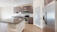 Located at 13650 Marsh View Blvd in Rogers, MN, this well-designed two-bedroom, one-bathroom residence offers a thoughtful single-floor layout with a comfortable and functional living experience. The open-concept kitchen and living area serves as the heart of the home, showcasing rich dark-toned cabinetry, granite countertops, a white subway tile backsplash, and a full suite of stainless steel appliances including a range, microwave, and refrigerator. A central kitchen island with built-in wine storage and a granite top provides additional prep and dining space. Light hardwood-style flooring flows throughout the main living areas, adding warmth to the neutral color palette. The living room is bright and airy, filled with natural light and anchored by sliding glass doors that open to a private balcony overlooking a landscaped green lawn. Both bedrooms are carpeted and well-lit, with the generously sized primary bedroom featuring a walk-in closet outfitted with wire shelving. The full bathroom includes a granite-topped vanity with dark cabinetry, a soaking tub, and light wood-look flooring. Additional highlights include a dedicated in-unit laundry area with a top-load washer, a pantry with a frosted-glass door, and a utility room, making this a highly practical and comfortable home.