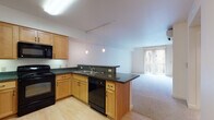 Located at 2751 Shadow View Dr in Eugene, Oregon, this single-floor unit offers a well-organized, open-concept layout designed for comfortable everyday living. The kitchen serves as a central feature, outfitted with warm maple cabinetry, dark granite countertops, and a full suite of black appliances including a range, built-in microwave, refrigerator, and dishwasher. Light hardwood-style flooring runs throughout the kitchen area, while pendant lighting and a track lighting system provide targeted illumination. A peninsula counter with an extended bar top creates a natural transition into the adjoining living area, which is finished with neutral carpet and benefits from abundant natural light through a large sliding glass door fitted with vertical blinds. The sliding door leads to an outdoor space, offering a pleasant connection to the exterior. A bedroom features carpet flooring, a window with outdoor views, and a distinctive two-tone accent wall. The bathroom includes a wood vanity with granite countertop, a tub-shower combination, and is conveniently situated adjacent to an in-unit stacked washer and dryer. Throughout the space, the clean, neutral palette and functional design elements contribute to a calm, move-in-ready atmosphere.