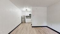 Located at 1255 S SH 6 Access Rd in Houston, TX, this single-floor unit offers a clean, functional layout designed for efficient living. The main living area is bright and open, finished with light wood-style vinyl plank flooring and crisp white walls that create an airy, welcoming atmosphere. A textured ceiling and a modern sputnik-style light fixture add a subtle contemporary touch to the space.

The kitchenette is thoughtfully appointed with white shaker-style cabinetry, a mosaic tile backsplash in neutral gray tones, a stainless steel refrigerator, an integrated microwave, and a single-basin sink — providing all the essential amenities in a compact footprint. The layout allows the kitchenette to flow naturally into the main living area, maximizing the sense of openness.

The bathroom features a full tub and shower combination with floor-to-ceiling white tile surround, brushed nickel fixtures, and matching wood-style flooring that ties the space together cohesively. A towel bar and built-in shelf add practical convenience.

A window near the entry door allows natural light into the living area, while a wall-mounted HVAC unit ensures year-round climate control. The unit's clean, updated finishes and efficient use of space make it a practical and comfortable option in the Houston area.