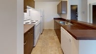 This single-floor residence features two bedrooms and one bathroom across a well-organized floor plan. The layout is practical and functional, with each area clearly defined. The living room is generously proportioned, finished with neutral carpet and anchored by a large window that frames views of surrounding greenery, filling the space with natural light. A baseboard heating system runs along the exterior wall, ensuring year-round comfort.

The galley-style kitchen is efficiently designed, featuring dark wood cabinetry, wood-toned countertops, and tile flooring. White appliances — including a range, refrigerator, and dishwasher — are included. A peninsula counter connects the kitchen to the living area, creating an open flow between the two spaces. The entry door is positioned conveniently adjacent to the kitchen.

Both bedrooms are carpeted and bright, each featuring windows with outdoor views and baseboard heating. The rooms offer a clean, neutral palette suitable for a variety of furnishing arrangements.

The bathroom includes tile flooring, a wide vanity with a marble-style countertop, lighted mirror, and white cabinetry. A closet with louvered doors is located nearby, providing additional storage. Overall, the space maintains a clean, functional character throughout.
