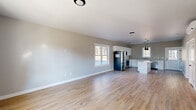 This newly built single-floor home offers a clean, modern aesthetic with an open-concept design that seamlessly connects the living area and kitchen. Light-toned hardwood flooring runs throughout, complementing the neutral gray and beige wall palette that gives the home a bright, airy feel.

The kitchen is a standout feature, outfitted with crisp white shaker-style cabinetry, white quartz countertops, a classic subway tile backsplash, and a full suite of stainless steel appliances including a French door refrigerator, range, microwave, and dishwasher. A center island provides additional prep and gathering space, while bold black pendant lighting adds a modern contrast. A stainless steel undermount sink is positioned beneath a window with views of the surrounding landscape.

The bedrooms are generously sized, filled with natural light from well-placed windows, and feature the same hardwood flooring. One bedroom includes a wall-mounted mini-split unit for independent climate control. The bathrooms are finished with clean, functional fixtures — one offering a tub-shower combo and another a standalone walk-in shower with a white vanity and tile flooring.

The entryway is welcoming with a paneled white front door and an adjacent window that draws in natural light, completing this move-in-ready home.