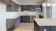 Located at 1185 Shelburne Road in Burlington, Vermont, this single-floor unit offers a clean, modern aesthetic throughout. The open living area is finished with wide-plank hardwood-style flooring that runs seamlessly across the space, complemented by crisp white walls and a wall-mounted mini-split system for efficient climate control. A large triple-pane window floods the room with natural light and provides views of the surrounding Vermont landscape, including mature trees and the open sky.

The kitchen is thoughtfully appointed with rich, dark-stained cabinetry featuring shaker-style doors and sleek hardware. Light quartz countertops provide a striking contrast, while stainless steel appliances — including a dishwasher and over-the-range microwave — add a contemporary touch. A kitchen island offers additional prep and counter space, and a dedicated pantry closet with built-in shelving provides generous storage just steps away.

The bathroom is finished with the same attention to detail, featuring a wide vanity with dark cabinetry, a white countertop, a large mirror, and a combined shower and tub. The overall design of this unit prioritizes functionality and modern style, making it a well-appointed space in a convenient Burlington location.