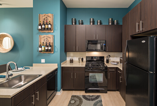 Classic Package II kitchen with black appliances, beige laminate countertops, dark brown cabinetry, white tile backsplash, and hard surface flooring - Avalon at Wesmont Station