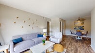 This single-floor residence offers a thoughtfully designed layout encompassing two bedrooms, two bathrooms, a combined living and dining area, a kitchen, a hallway, and a closet. The living room showcases warm wood-look flooring, neutral gray walls, and a mid-century modern aesthetic, with open sightlines connecting to the dining area. The dining space is accented by a ceiling fan and colorful wall art, creating a bright and inviting atmosphere ideal for everyday meals or entertaining. The kitchen features dark espresso cabinetry paired with light quartz-style countertops, a white subway tile backsplash, and black appliances, delivering a striking contrast that is both stylish and functional. The primary bedroom offers plush carpeting, natural light through large windows with decorative curtains, and ample space for a full bedroom suite. The second bedroom mirrors this comfortable aesthetic with carpet flooring and a bright window. Both bathrooms are finished with white subway tile wainscoting, dark vanity cabinetry, light countertops, and framed mirrors, offering a clean and classic look. Throughout the residence, the cohesive design palette of soft grays, warm wood tones, and modern fixtures creates a comfortable and contemporary living environment.