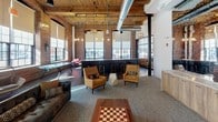 Located at 220 Merrimack in Lawrence, Massachusetts, this single-floor amenity space masterfully blends historic industrial character with modern design. Original exposed brick walls, soaring wood-beam ceilings, and sweeping arched openings serve as the architectural backbone of the space, while large multi-pane windows flood the interior with abundant natural light and frame views of the surrounding area.

The expansive open layout is divided into distinct yet connected zones. A generous lounge area features tufted leather sofas, accent chairs, and geometric stone side tables arranged around a central carpeted gathering area, complemented by a dramatic built-in fireplace with a textured tile surround and ambient accent lighting. Pendant and track lighting hang from the exposed-beam ceiling, adding warmth to the industrial aesthetic.

A central bar area with dark countertops and barstool seating serves as a social hub, while a well-appointed kitchenette offers warm wood cabinetry, a herringbone marble tile backsplash, quartz countertops, stainless steel appliances including a built-in oven, microwave, refrigerator, and a deep undermount sink. Additional recreational areas, including a pool table, round out the amenities. The combination of hardwood and polished floors anchors the space's rich, layered character.