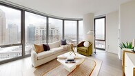 Located at 1001 South State Street in Chicago's South Loop neighborhood, this thoughtfully designed two-bedroom, two-bathroom residence offers a bright, modern living experience across a well-planned single floor. Light hardwood flooring flows throughout, complemented by a clean, neutral palette that enhances the sense of openness.

The entry hallway sets an elegant tone, leading into a combined kitchen and living area that serves as the heart of the home. The kitchen features white cabinetry, a large island with bar seating, stainless steel appliances, a gas cooktop, and a stainless steel range hood, all framed by floor-to-ceiling windows with striking Chicago skyline views. The living area continues this panoramic experience with dramatic curved corner windows that flood the space with natural light.

The generously sized primary bedroom benefits from expansive city views through large windows, light wood floors, and a soft sage accent wall that adds warmth and character. The second bedroom offers a serene retreat with a neutral palette and direct hallway access. Both bathrooms are finished with large-format tile flooring, white vanity cabinetry, and mirrored medicine cabinets. Additional highlights include three closets, in-unit laundry, and a layout designed to maximize both comfort and functionality.